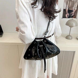 Black leather drawstring bucket bag with silver stud accents worn by model in white dress