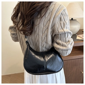 Close-up of a black crescent shoulder bag in glossy oil-wax leather on a model's shoulder