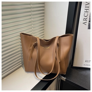 Detail of a brown leather tote bag with elegant metallic logo on a white window sill