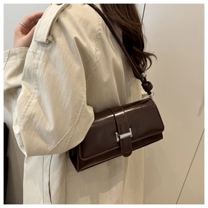 Detail of a dark brown baguette bag with a silver buckle worn with a beige trench coat