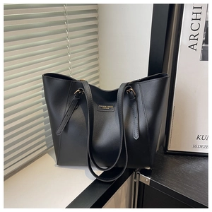 Detail of black faux leather tote bag with golden buckle and embossed fashion logo