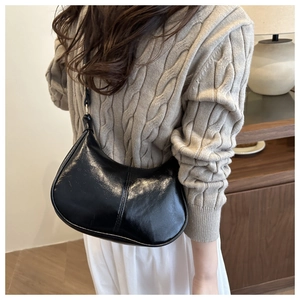 Detail of glossy black faux leather hobo bag worn with a beige knitted sweater