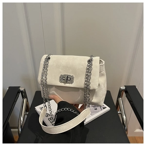 Detail of white suede crossbody bag with rhinestone buckle and silver chain on black chair