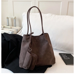 Detail of a large brown suede tote bag with a small zipper pouch on a white bedding background