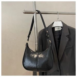Detail of black crescent shoulder bag featuring glossy PU leather and gold hardware buckle