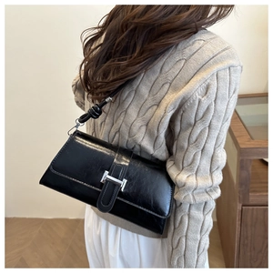 Détail d'un sac sous le bras noir brillant avec boucle en H argentée et bandoulière nouée