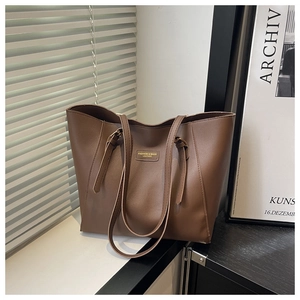 Detail of a large brown leather tote bag with gold stamped fashion text and long shoulder straps