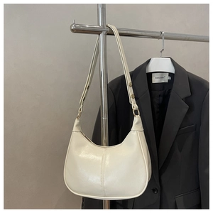 Detail of a minimalist off-white crescent bag hanging with a metallic buckle and strap