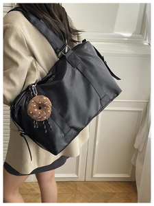 Détail d'un grand sac cabas en cuir noir avec des coutures solides et un charme donut