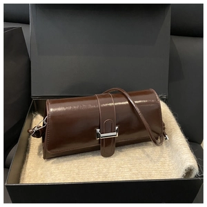 Detail of a shiny dark brown baguette bag with silver buckle in a gift box