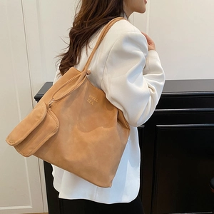 Brown faux suede large tote bag with a small coin purse worn by a model in a white suit