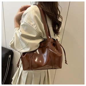 Detail of dark brown glossy bucket bag with drawstring closure and slim shoulder straps