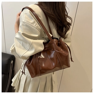 Detail of glossy brown crossbody bag with decorative drawstring bows and soft texture