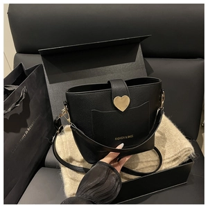 Close-up of black litchi leather bucket bag with gold heart buckle in luxury gift box