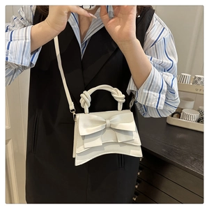 Détail du mini sac blanc avec un grand nœud, poignée nouée et base au design incurvé
