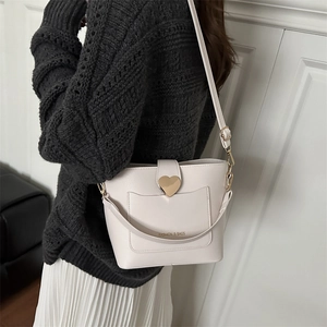Cream bucket bag with heart buckle and leather strap paired with a grey knit sweater