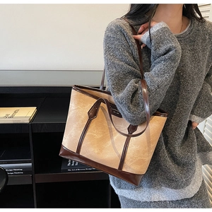 Detail of a large brown tote bag with contrast stitching carried by a model in a gray sweater