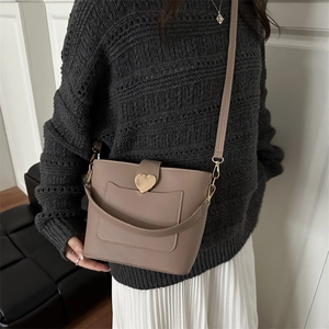 Chic tan textured leather bucket bag with gold heart clasp worn by a model in casual style