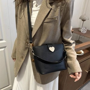 Chic black bucket crossbody bag with a golden heart clasp worn in a stylish home setting