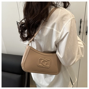 Detail view of a beige minimalist baguette bag featuring an embossed G logo on matte leather