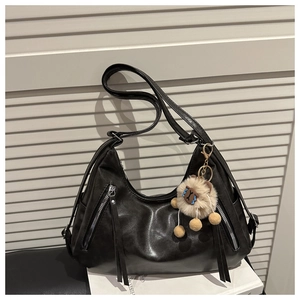 Detail of a black retro hobo bag with tassel zippers and a cute plush keychain charm