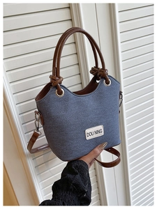 Détail du sac seau en denim bleu avec anses en cuir marron et étiquette de marque