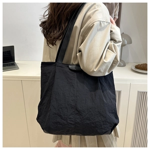 Detail of black pleated nylon tote bag with Fashion tag worn on shoulder in modern interior