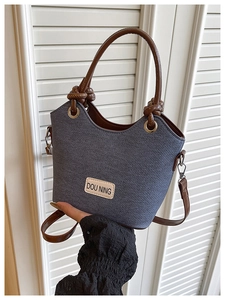 Détail du sac seau en denim gris avec poignées en cuir marron torsadées et étiquette