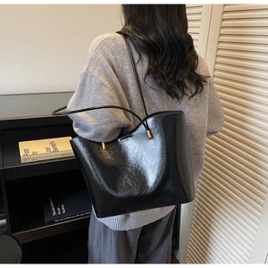 Detail of glossy black tote bag with gold hardware shown in a minimalist lifestyle setting