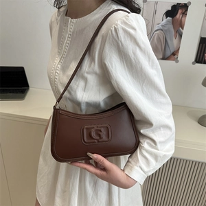 French style brown leather baguette bag with embossed G logo worn by a model in white