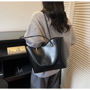 Detail of glossy black tote bag with slender leather straps and gold metal accents