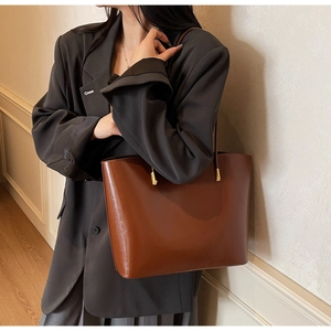 Detail of dark brown leather tote bag with elegant gold metal cylinder strap hardware