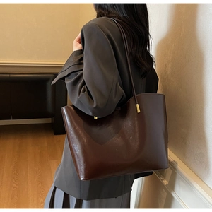 Detail of soft leather large brown tote bag on model shoulder in warm interior