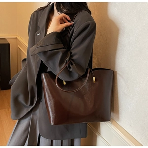 Deep brown faux leather tote bag detail with gold metal accents on long shoulder straps
