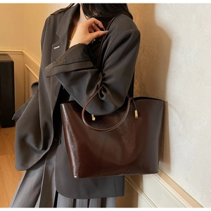 Deep brown glossy tote bag with slim straps and gold hardware worn by model