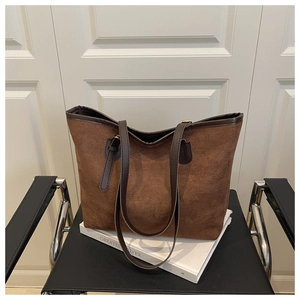 Détail d'un cabas en daim marron avec anses en cuir et boucles en métal doré sur chaise