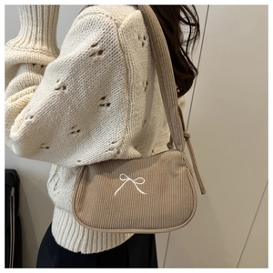 Detail of khaki corduroy underarm bag with white bow embroidery and knotted strap