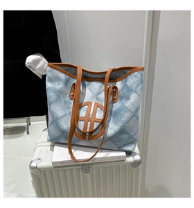 Blue plaid tote bag with brown leather handles placed on white suitcase for travel