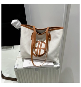 Detail view of large canvas tote bag with brown leather trim resting on a white suitcase