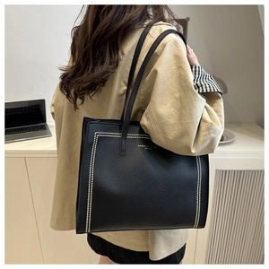 Detail of black pebbled leather tote bag with rivet frame and gold fashion branding