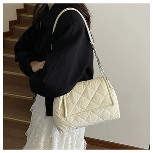 Detail of cream quilted shoulder bag with chain strap shown on a model in black outfit