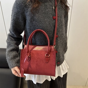 Retro red crossbody bag with dual handles and gold lettering shown in a stylish outfit