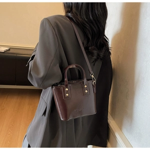 Detail of dark chocolate glossy leather bucket bag with gold rivets on grey blazer