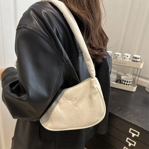 Chic beige corduroy handbag with pink bow embroidery worn over a black leather jacket