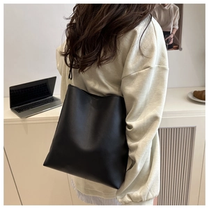 Minimalist black leather bucket bag shown being worn by a model in a modern home setting