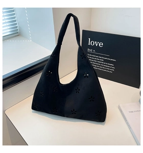 Detail of black suede tote bag featuring laser-cut floral patterns and wide shoulder strap