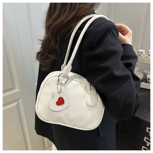 Detail of white lychee leather shoulder bag with a red heart pendant on a woman model