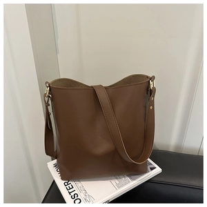 Detailed view of dark brown leather bucket bag with gold hardware and wide shoulder strap