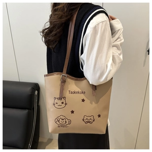 Khaki tote bag with cartoon cat print and adjustable strap shown on model's shoulder