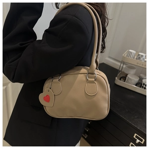 Detail of khaki pebbled leather shoulder bag with red heart charm on black blazer